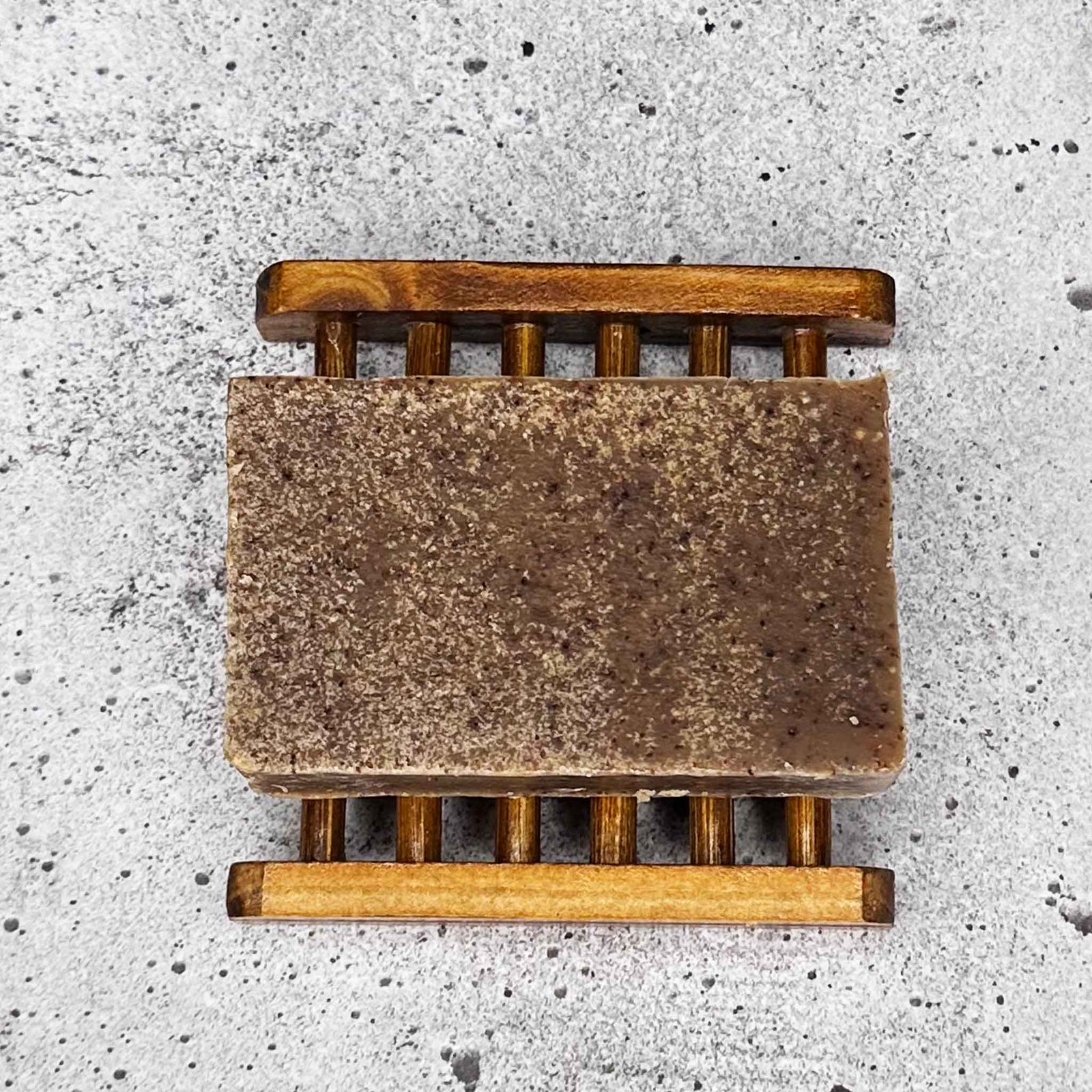 Bar of soap on a wooden soap dish against a concrete background
