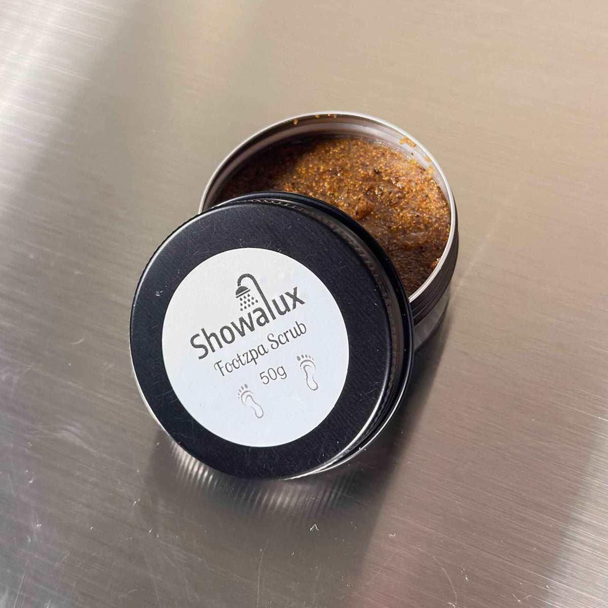 Showalux foot scrub in a black container on a metallic surface