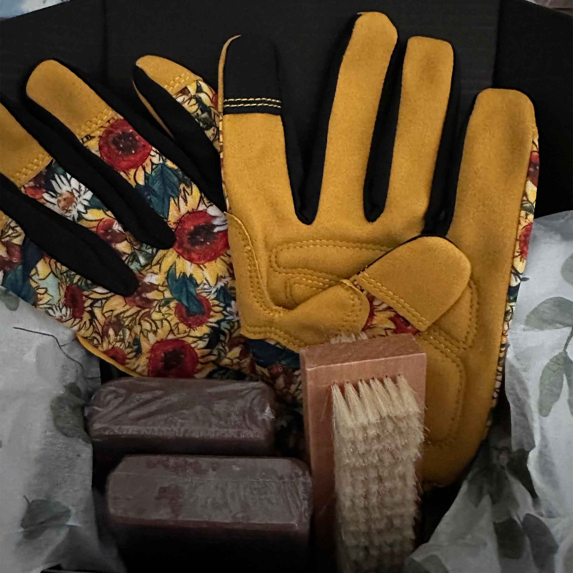 Pair of yellow gloves with floral pattern, scrubber, and soap bars on a dark background