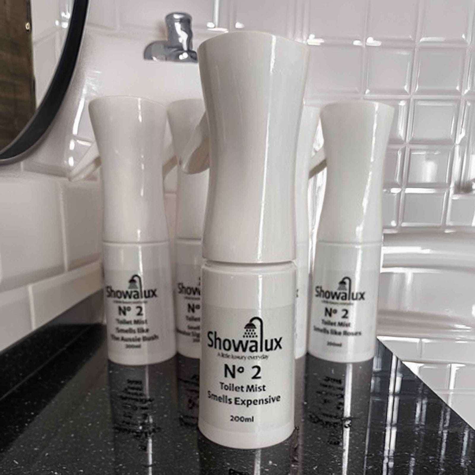 Five Showalux toilet spray mist bottles on a black surface with tiled wall background
