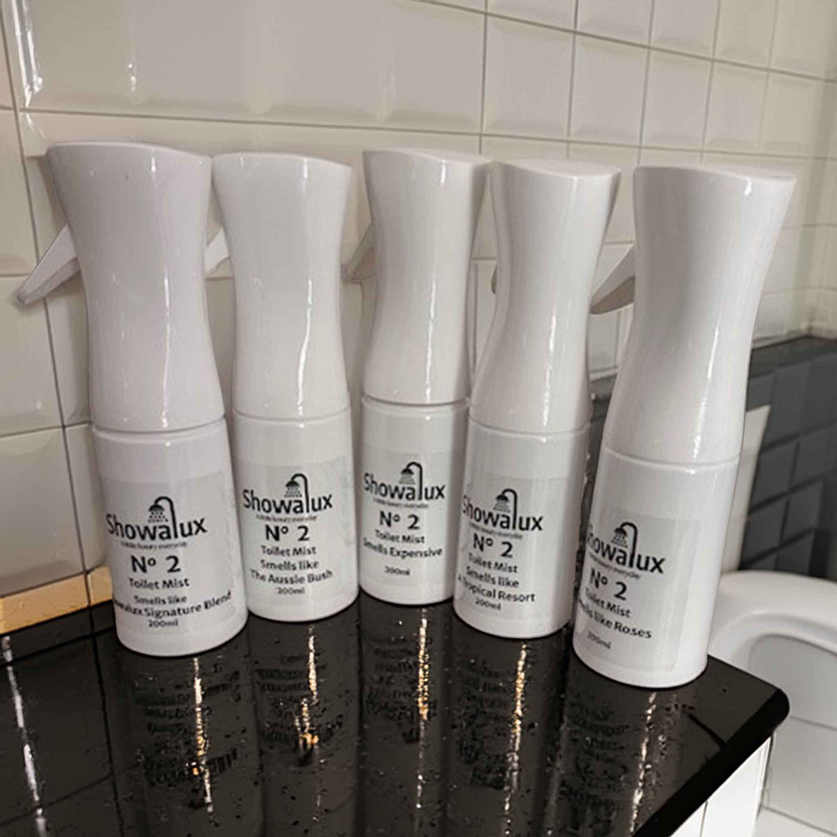 Five Showalux toilet spray mist bottles on a black surface with tiled wall background