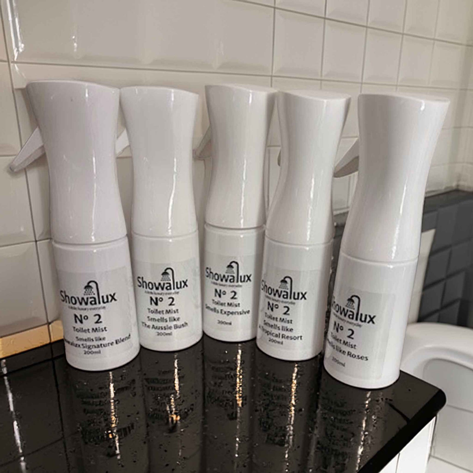 Five Showalux toilet spray mist bottles on a black surface with tiled wall background